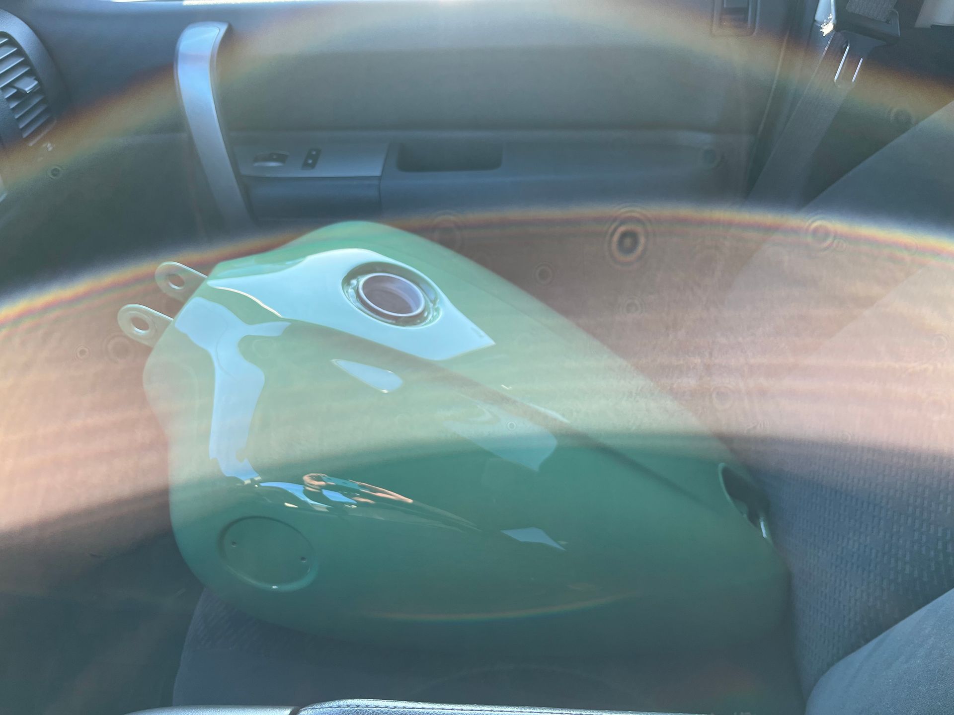A green motorcycle tank is sitting in the back seat of a car.