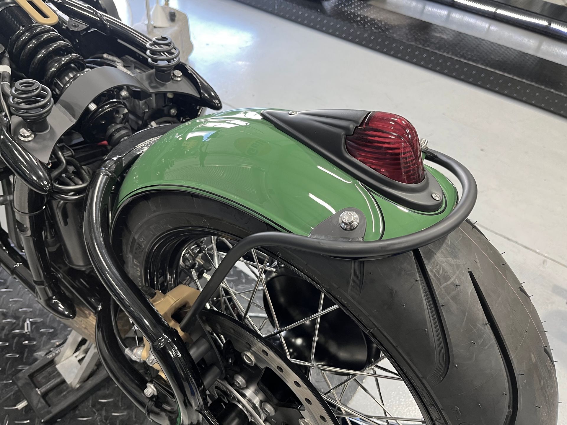 A green motorcycle with a red tail light is parked in a garage.