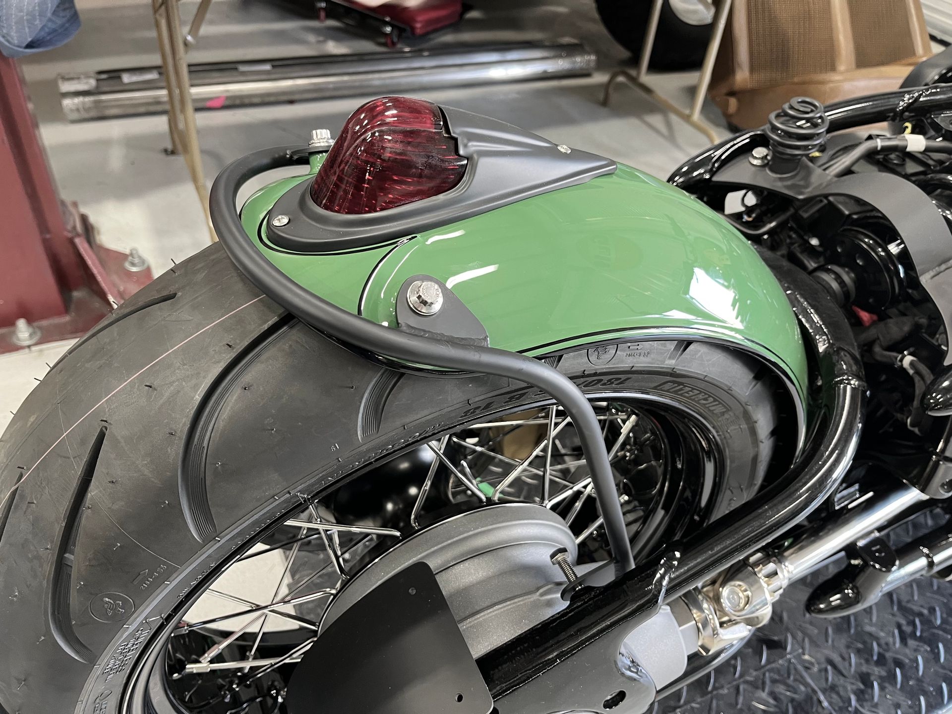 A green motorcycle with a red tail light is parked in a garage.