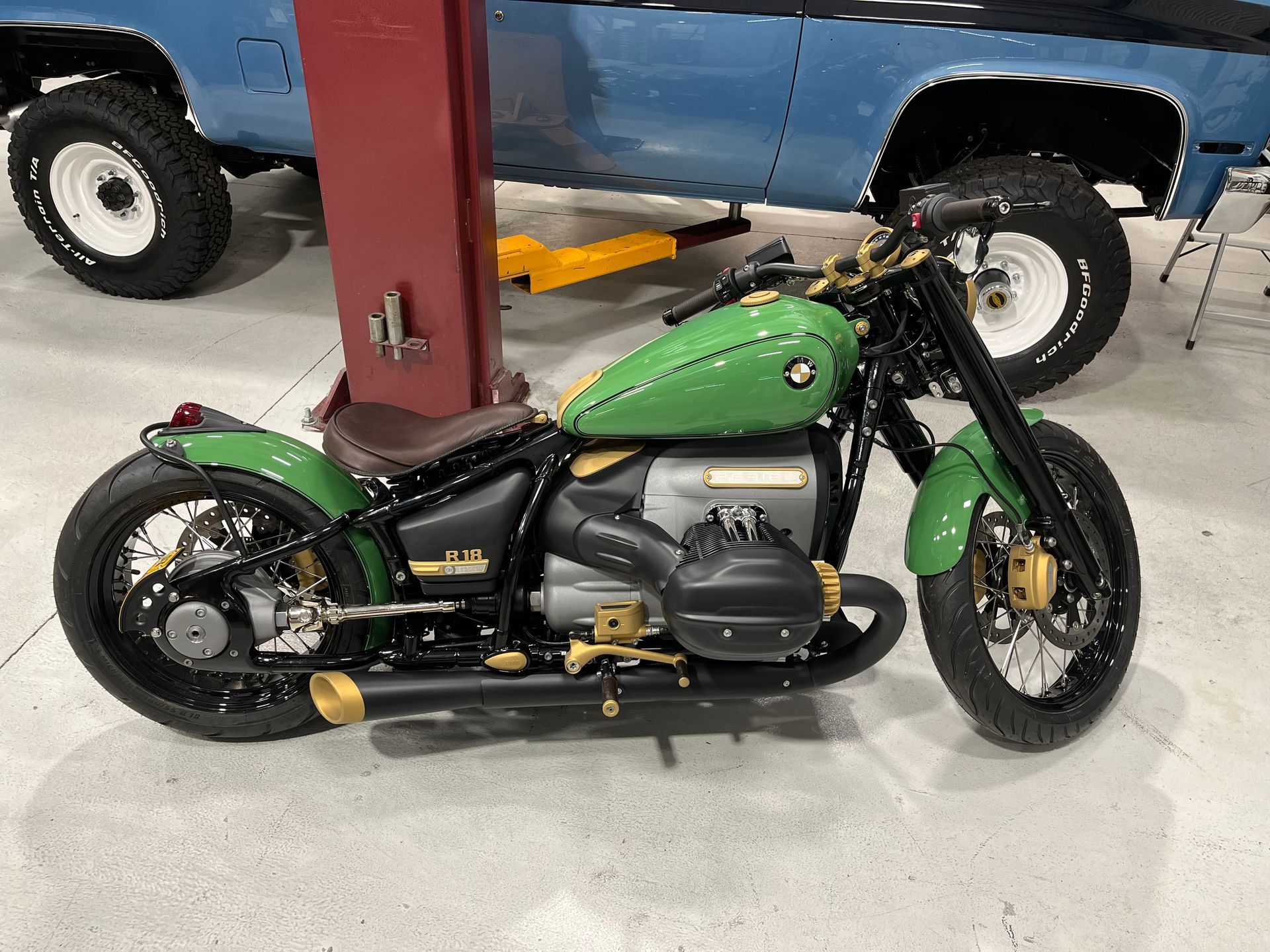 A green motorcycle is parked in a garage next to a blue truck.
