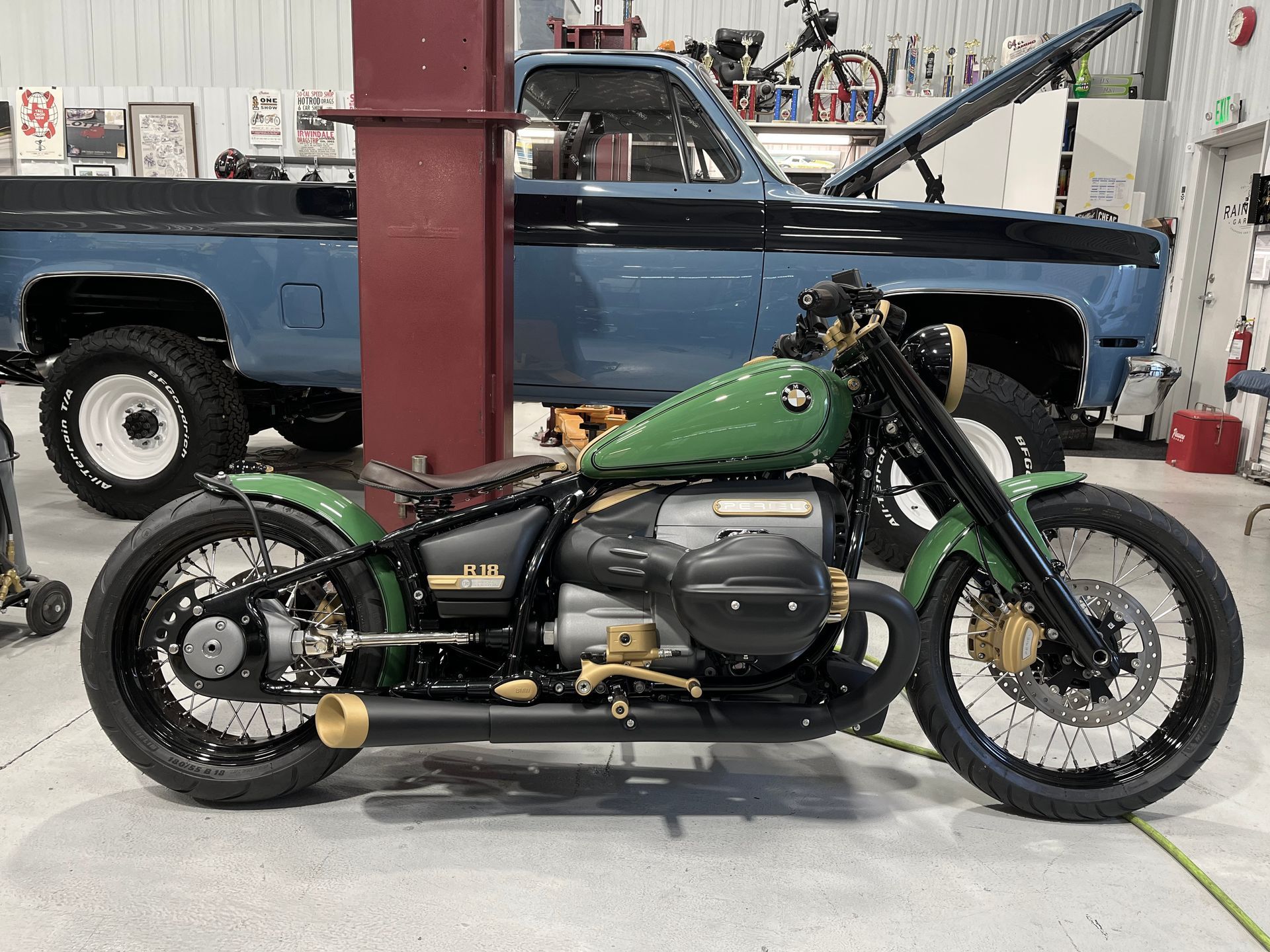 A green motorcycle is parked next to a blue truck in a garage.