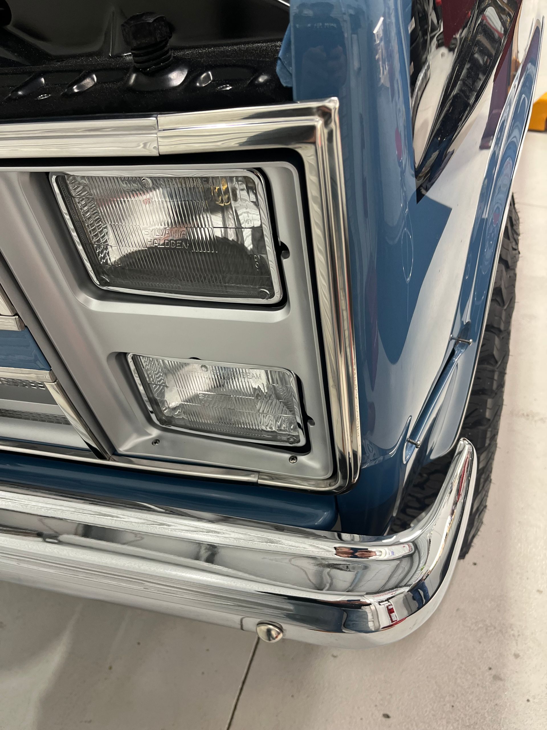 A close up of a blue truck 's headlights and bumper.