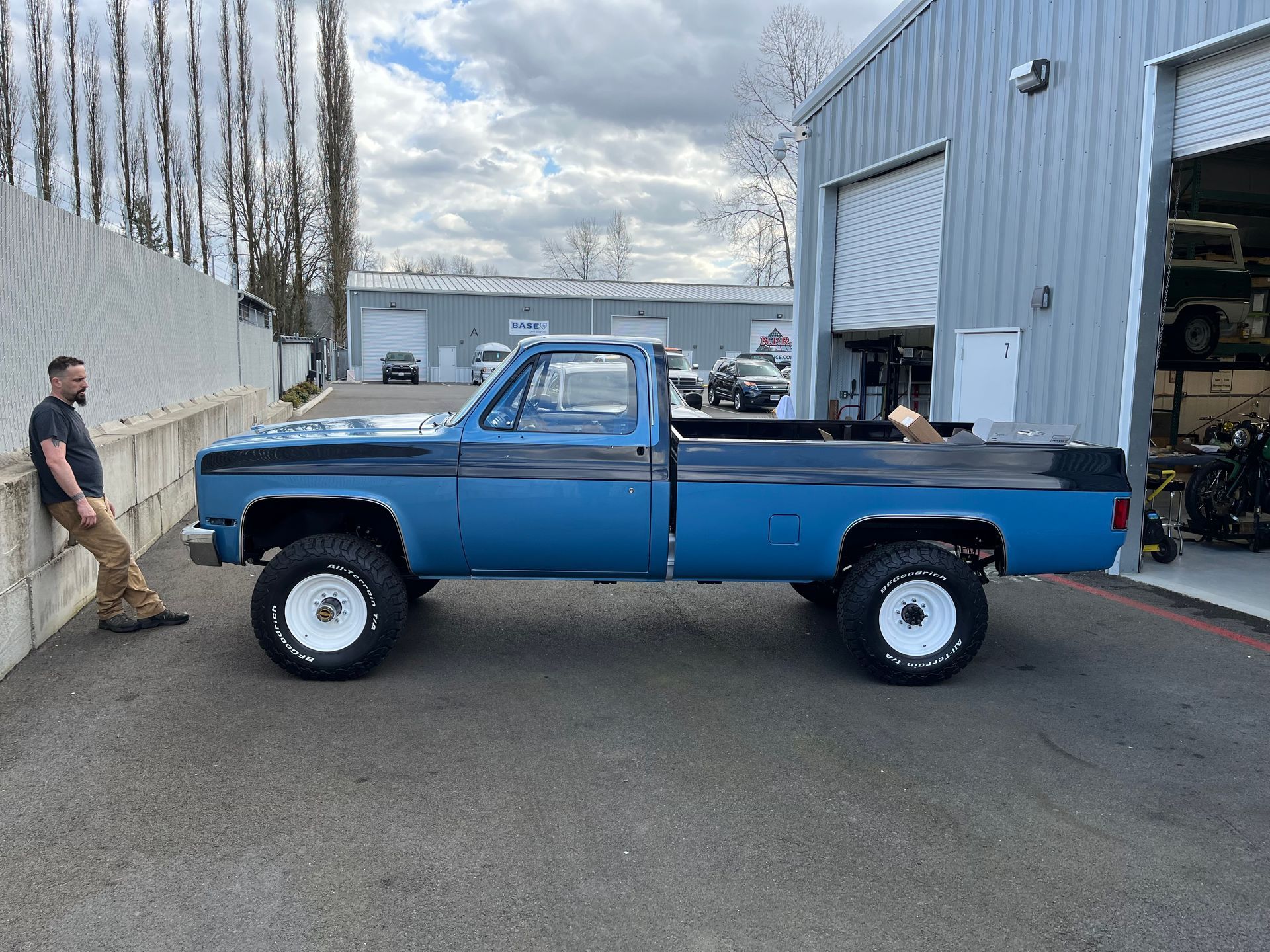 A man is leaning against a wall next to a blue truck.