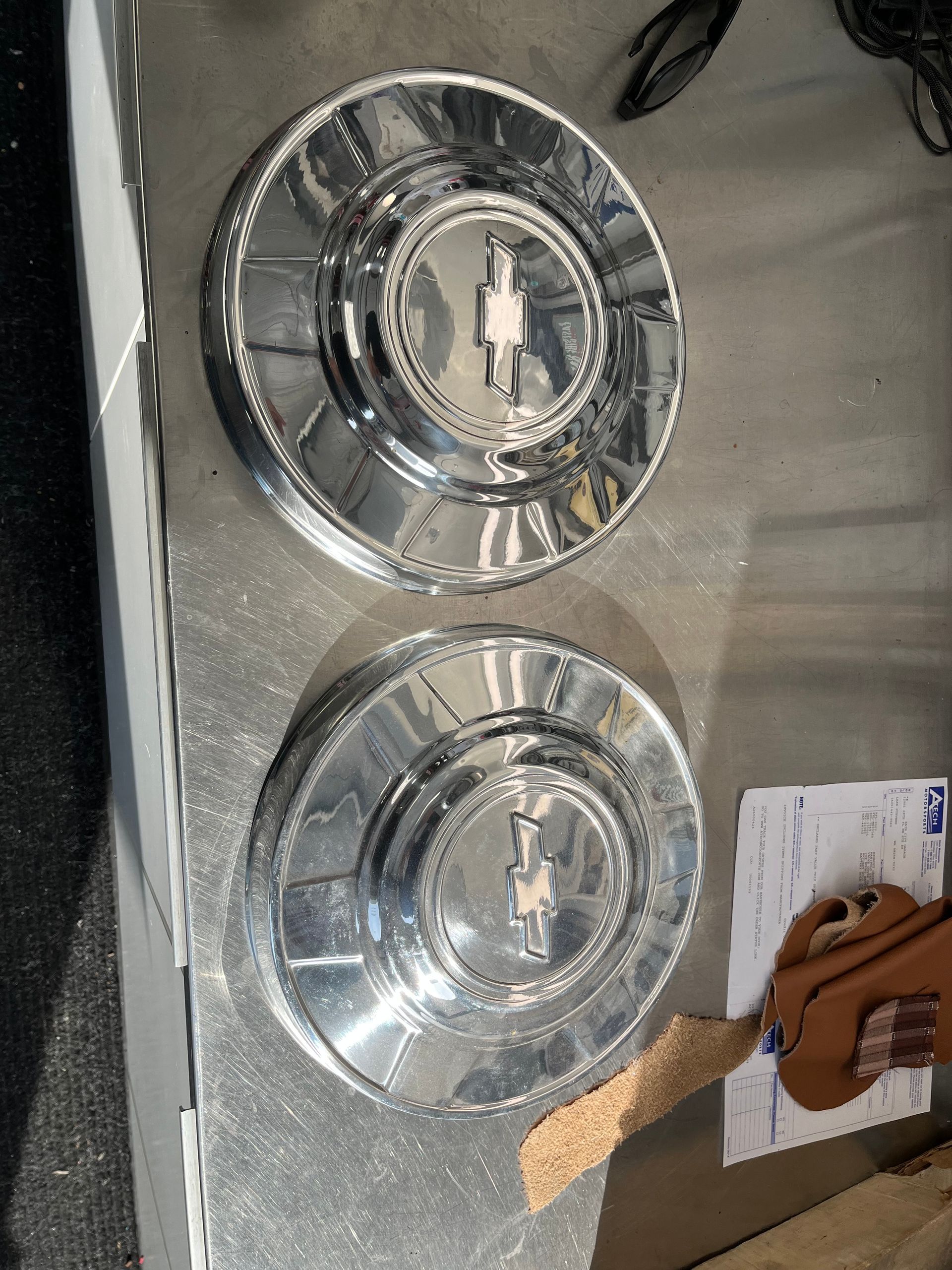 Two chrome wheel covers are sitting on top of a stainless steel table.