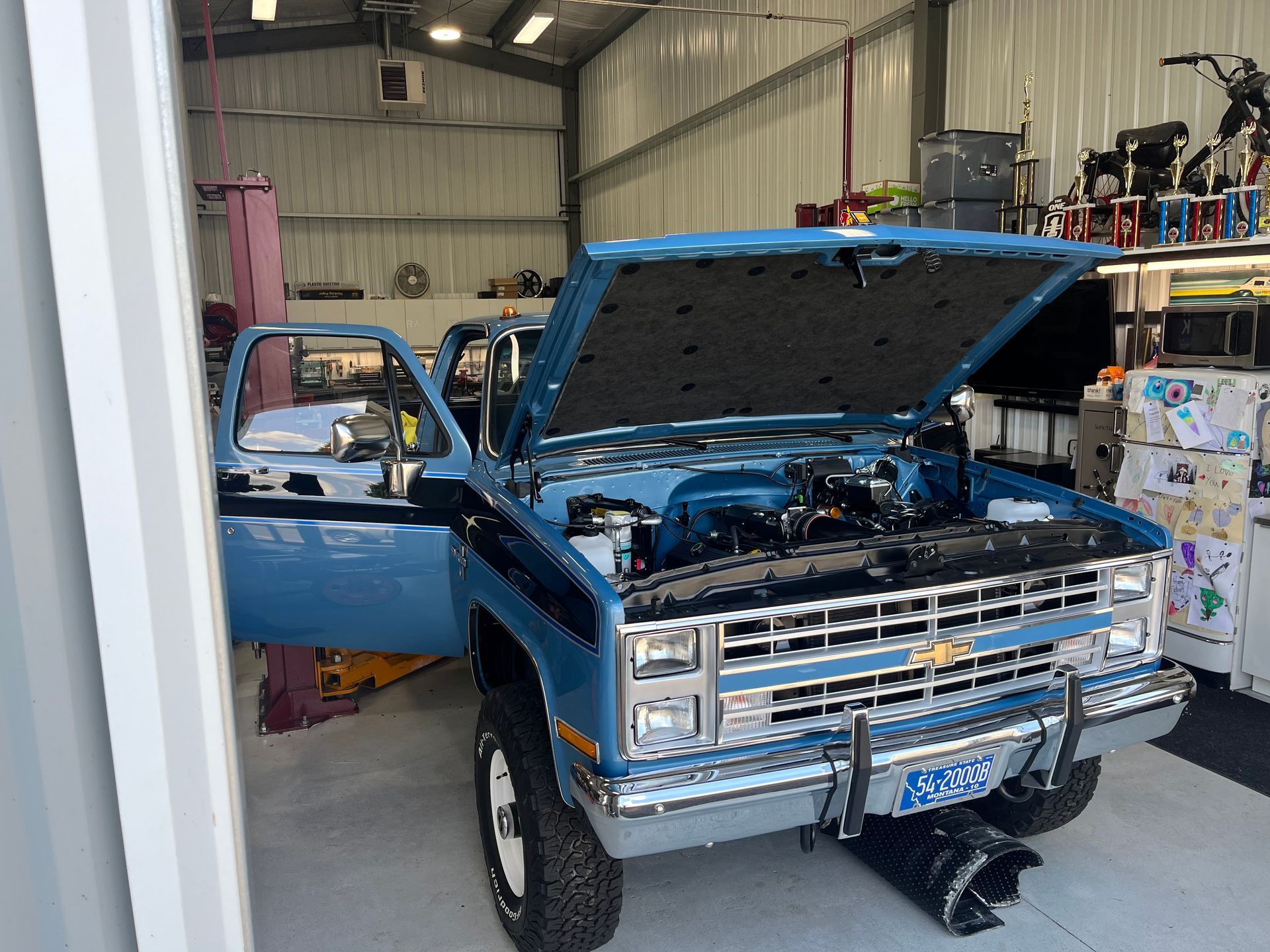 A blue truck with the hood up is in a garage.