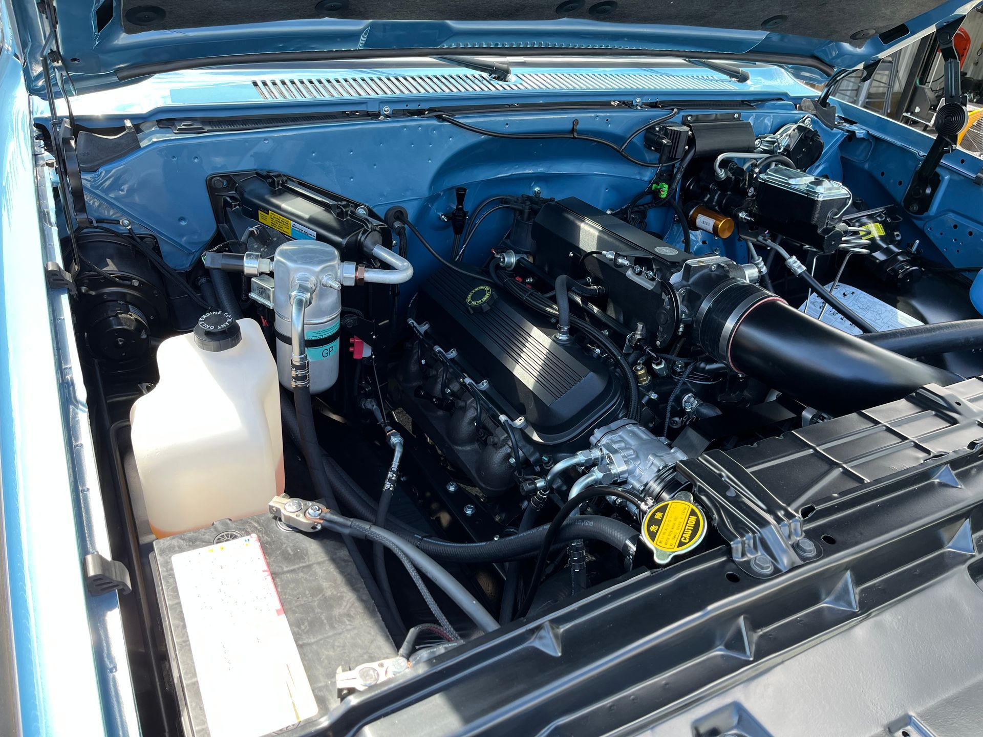 The engine of a blue car is shown with the hood open.