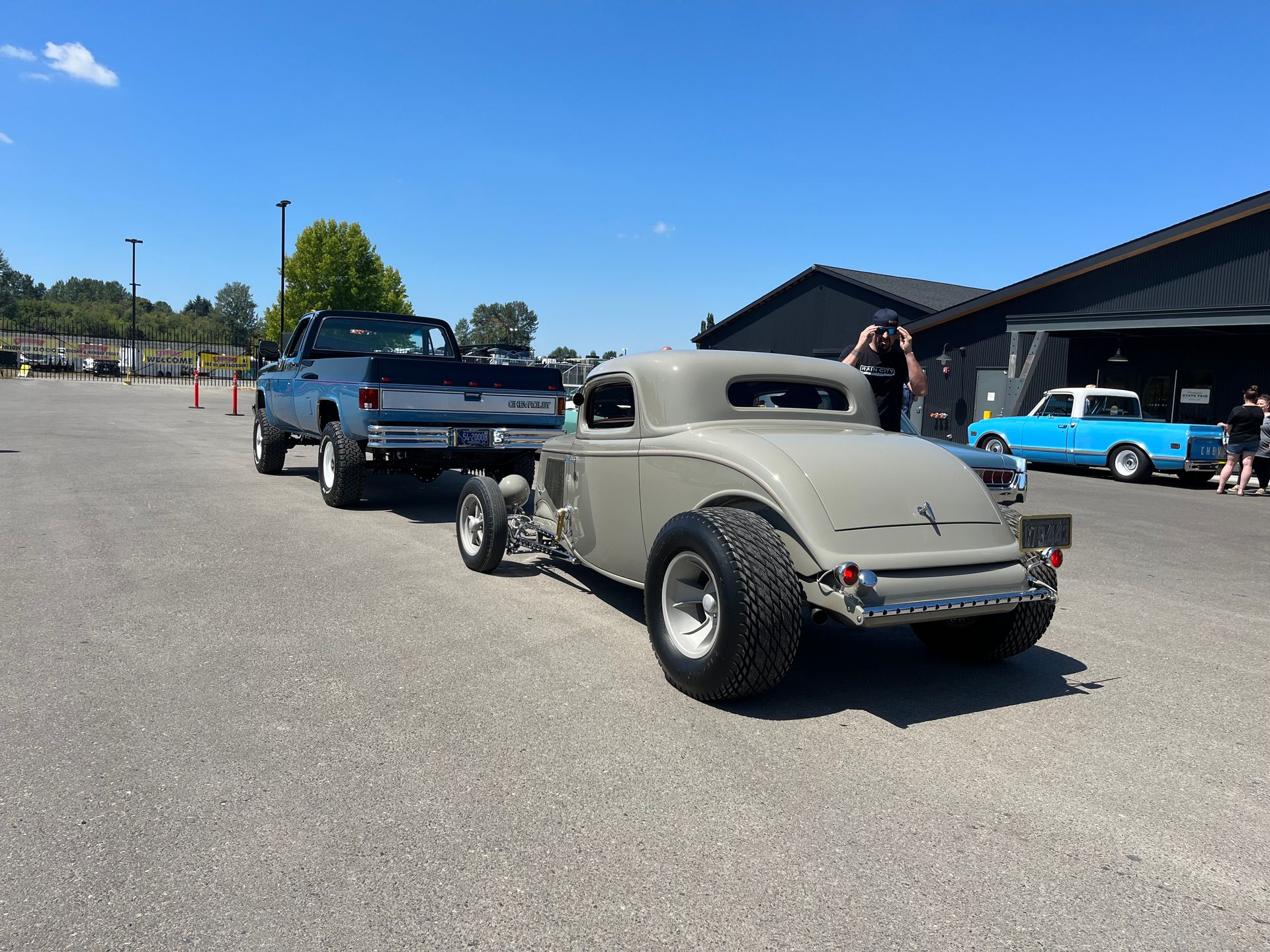 A hot rod is being towed by a truck in a parking lot.