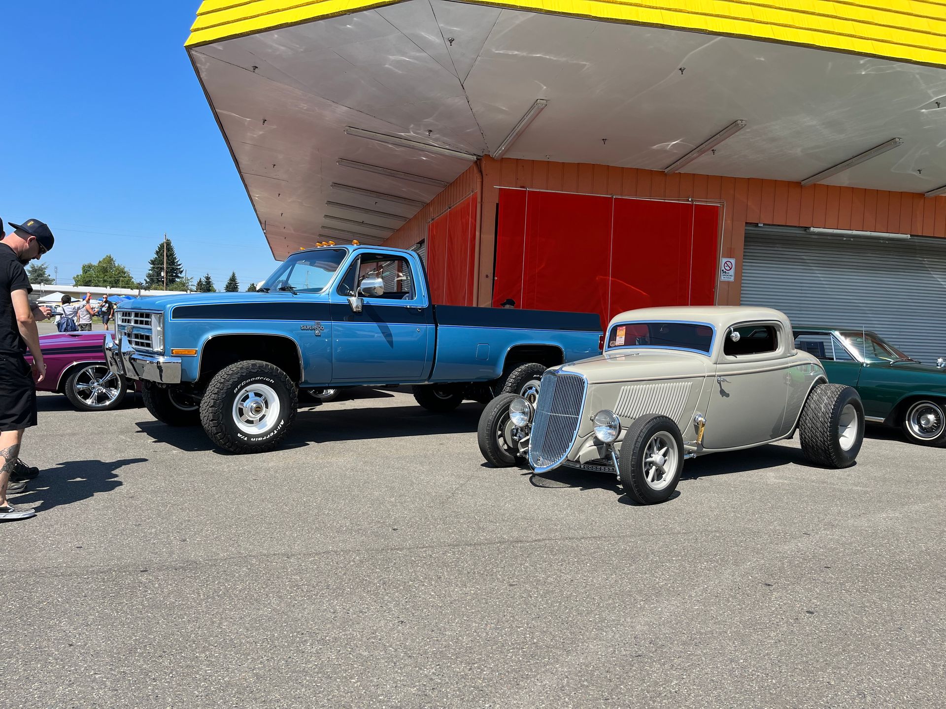 A blue truck and a grey car are parked in front of a building