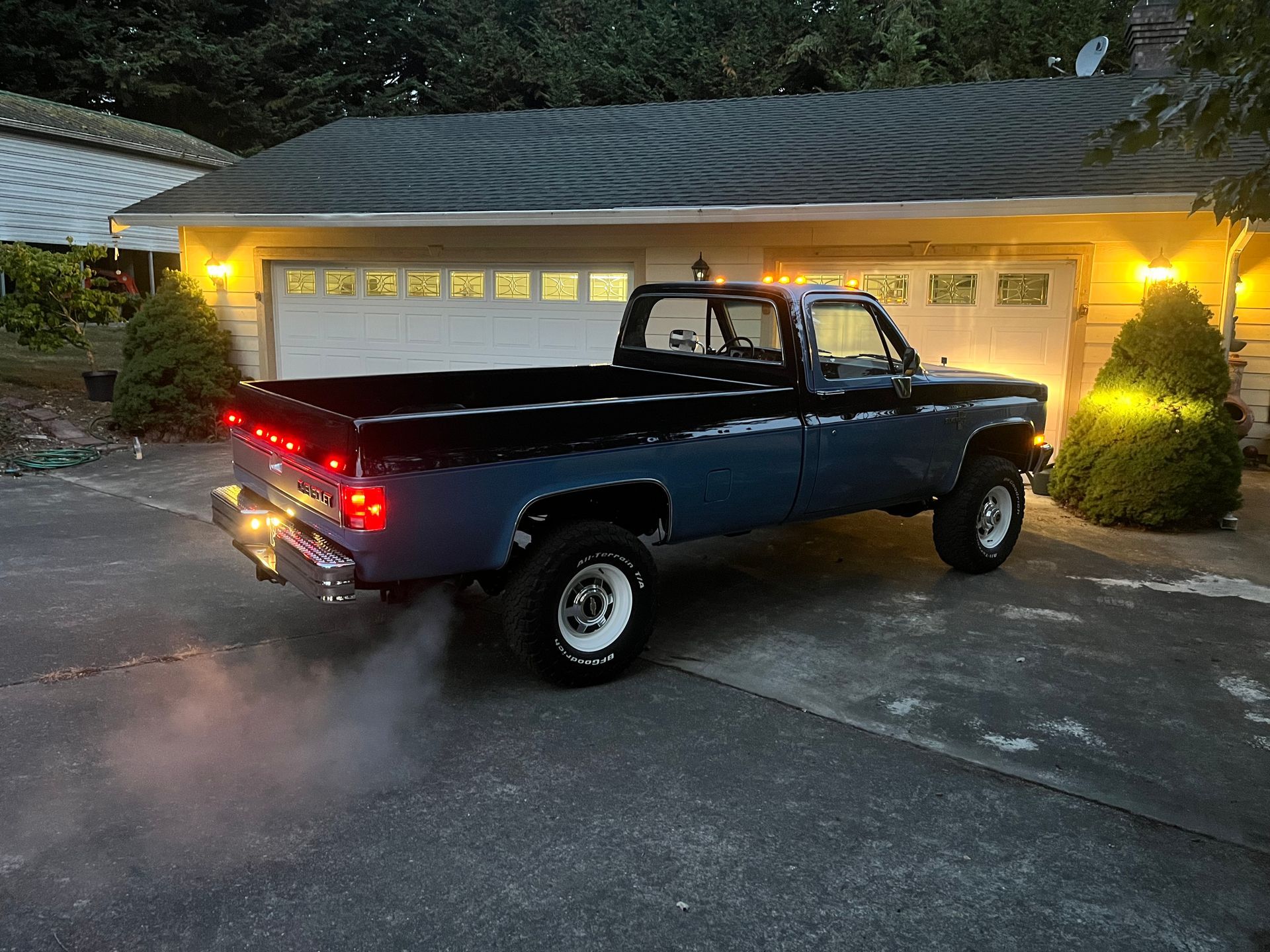 A blue truck is parked in front of a house at night.