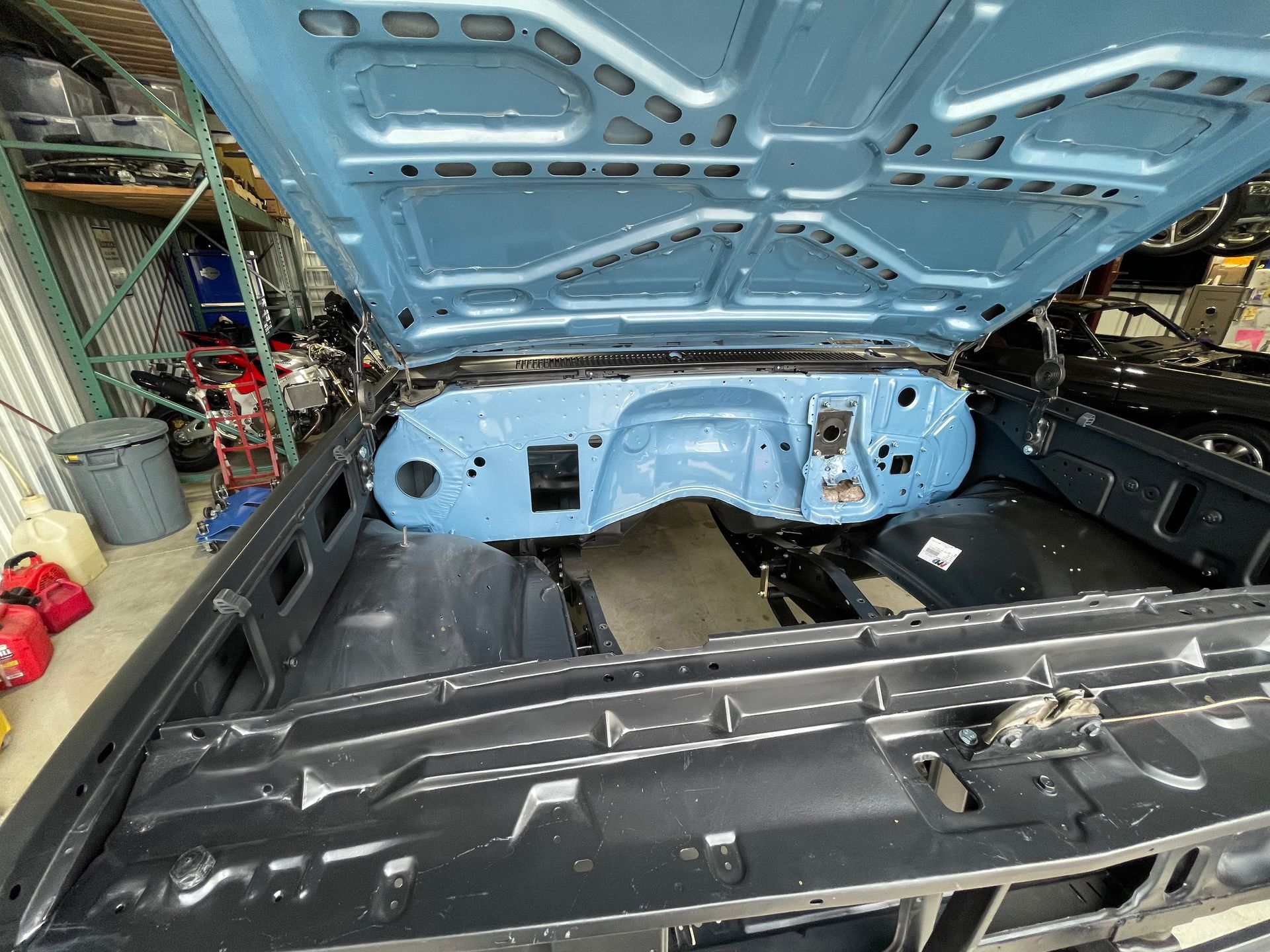 The hood of a blue car is open in a garage.