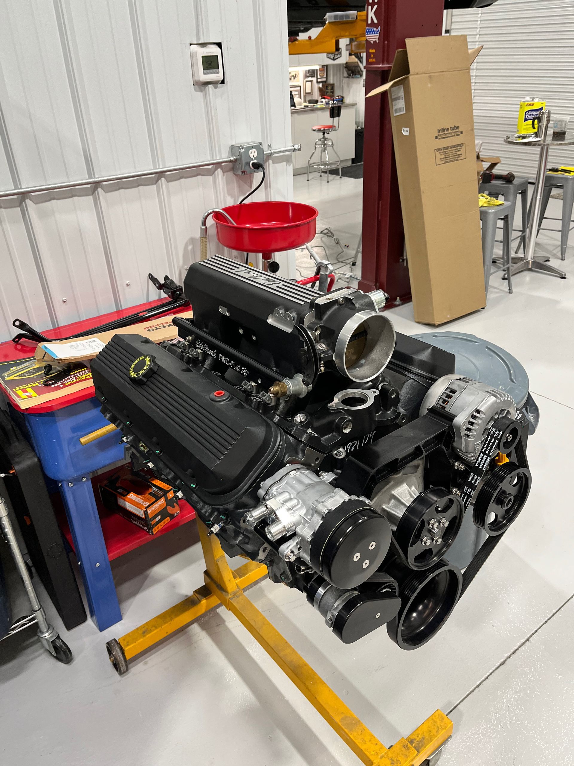 A black engine is sitting on top of a yellow stand in a garage.
