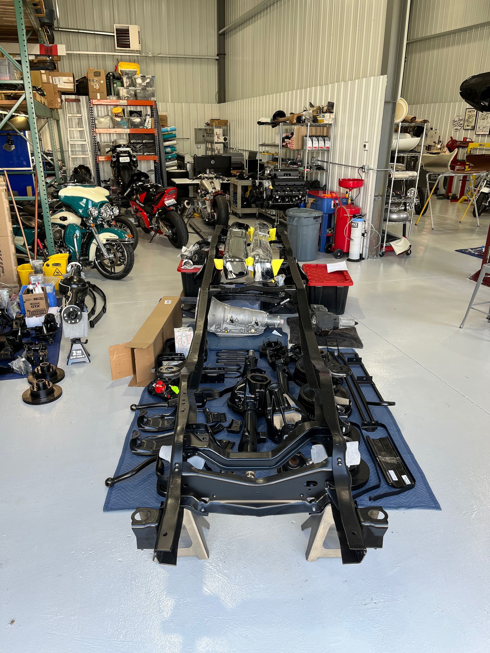 A car is being built in a garage with a lot of parts on the floor.