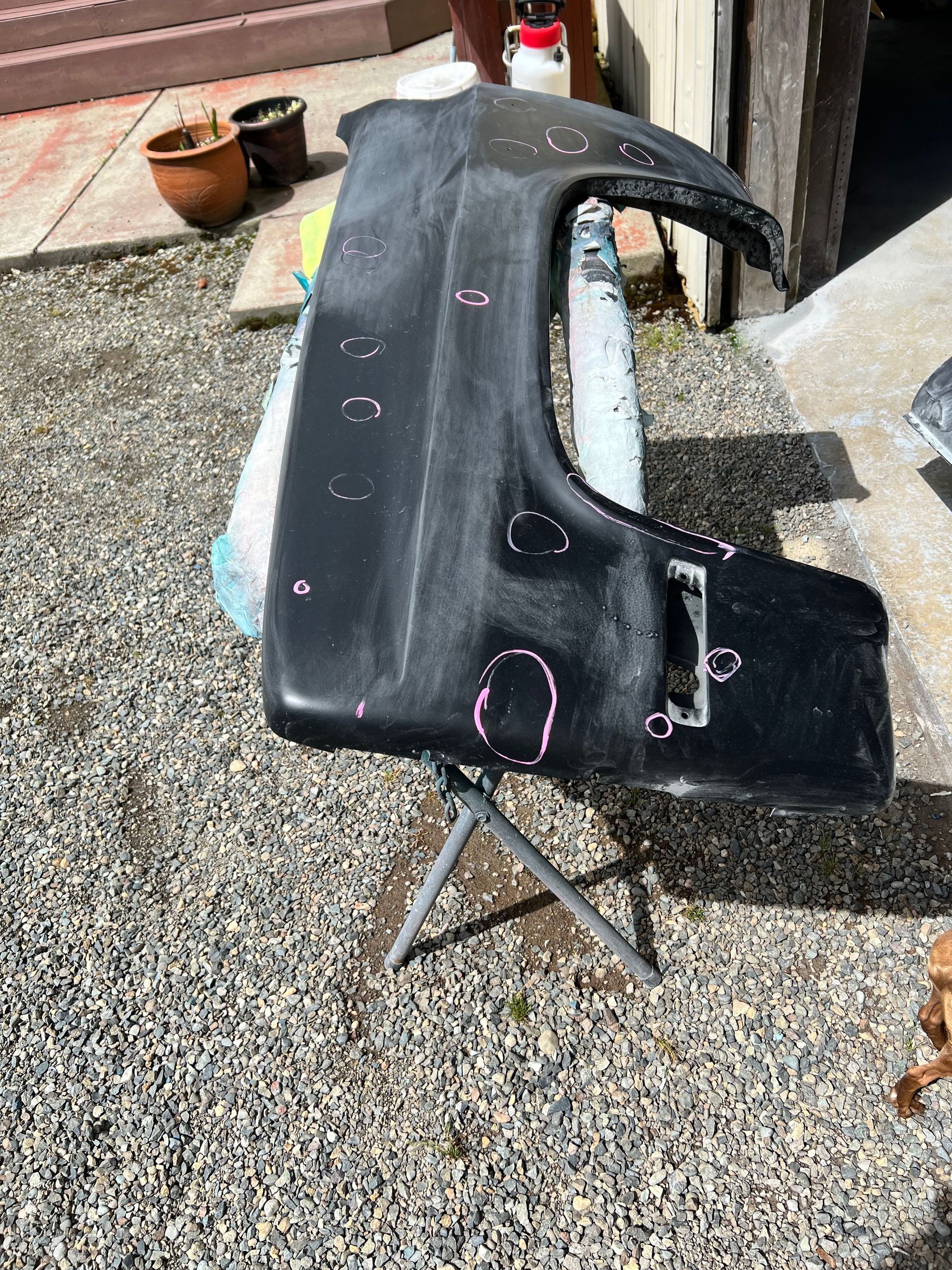 A black fender is sitting on a metal stand on gravel.