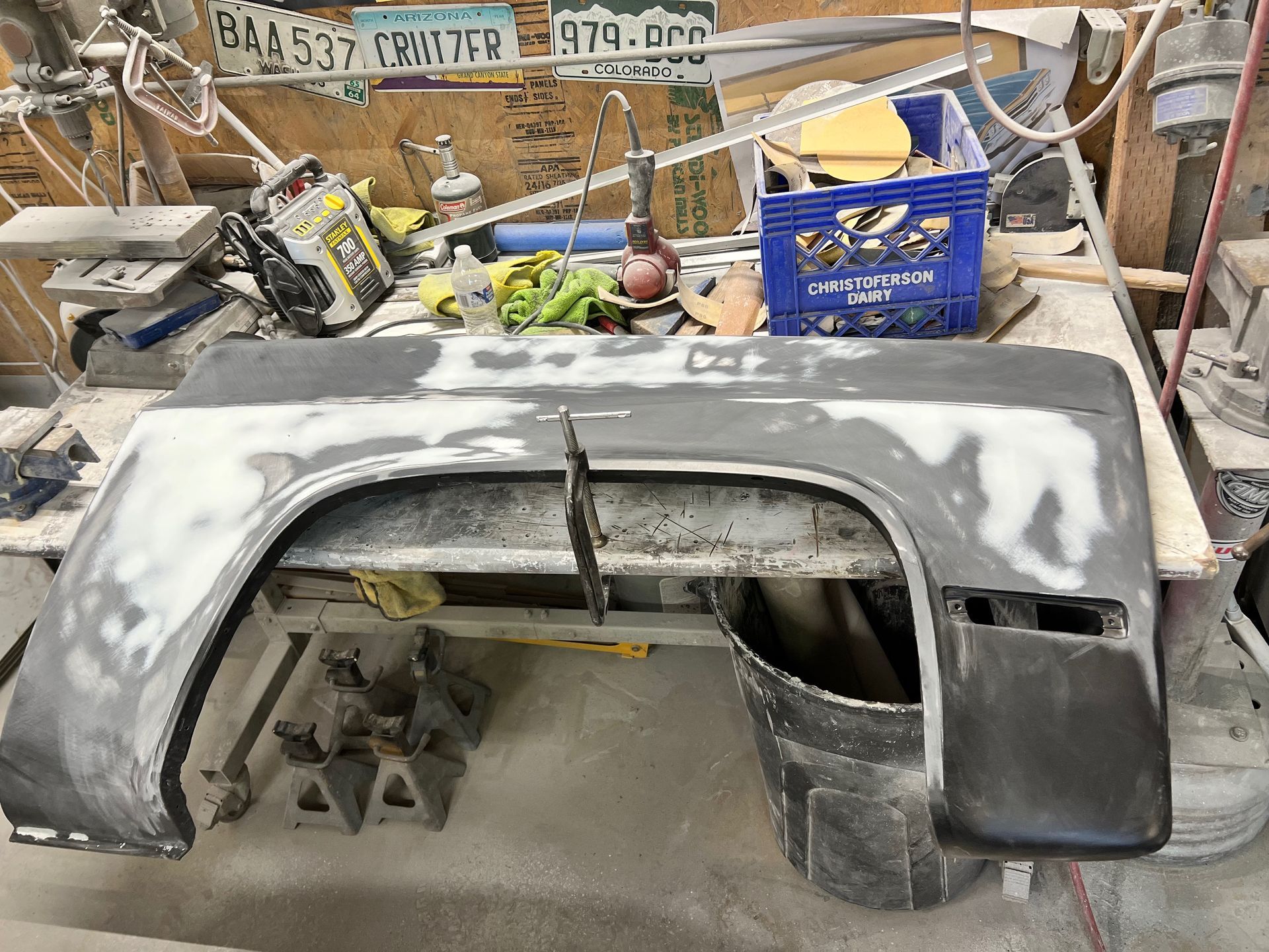 A fender is sitting on a table in a garage with a license plate that says 574-brb