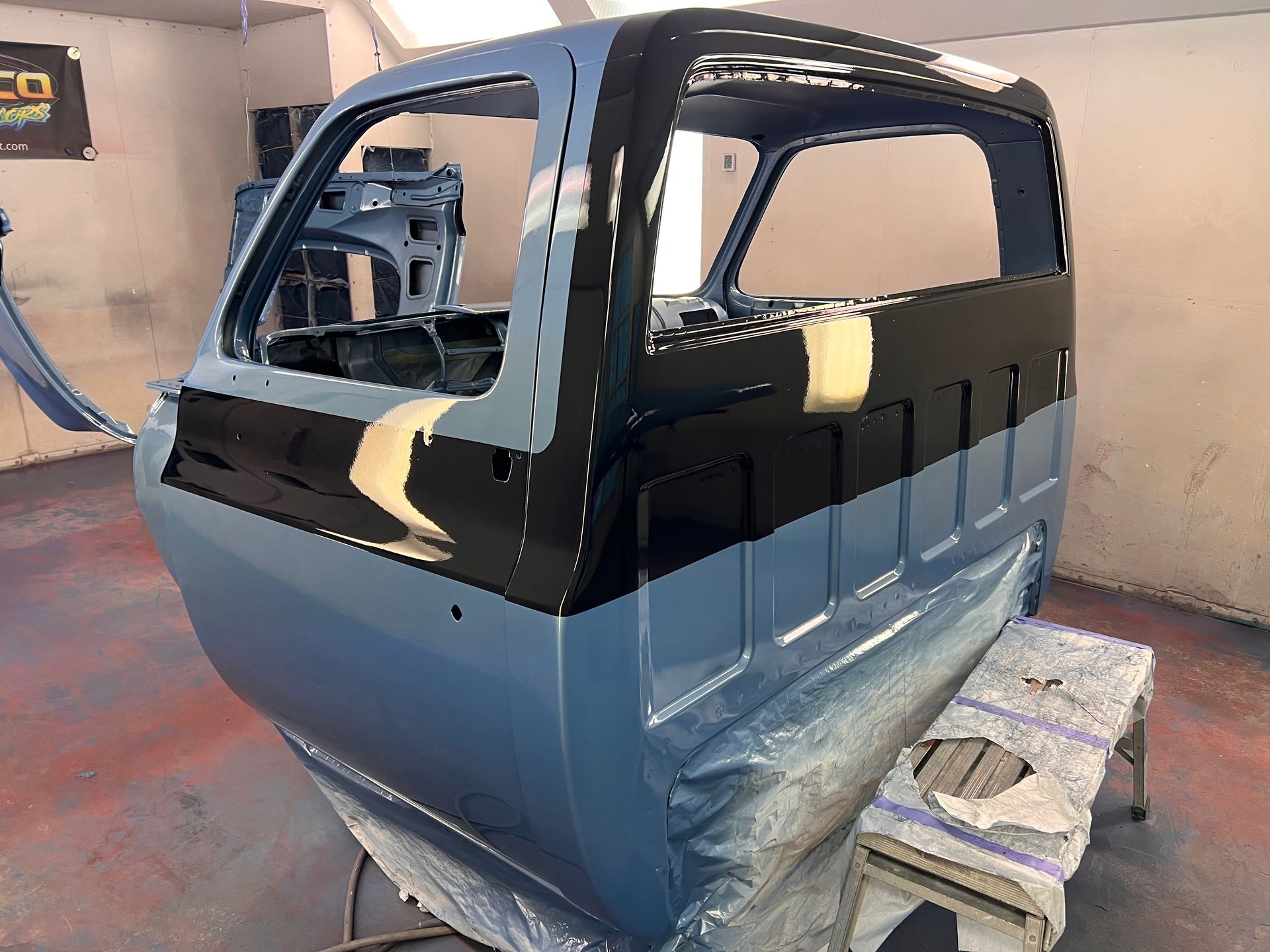 A blue and black truck is being painted in a garage.
