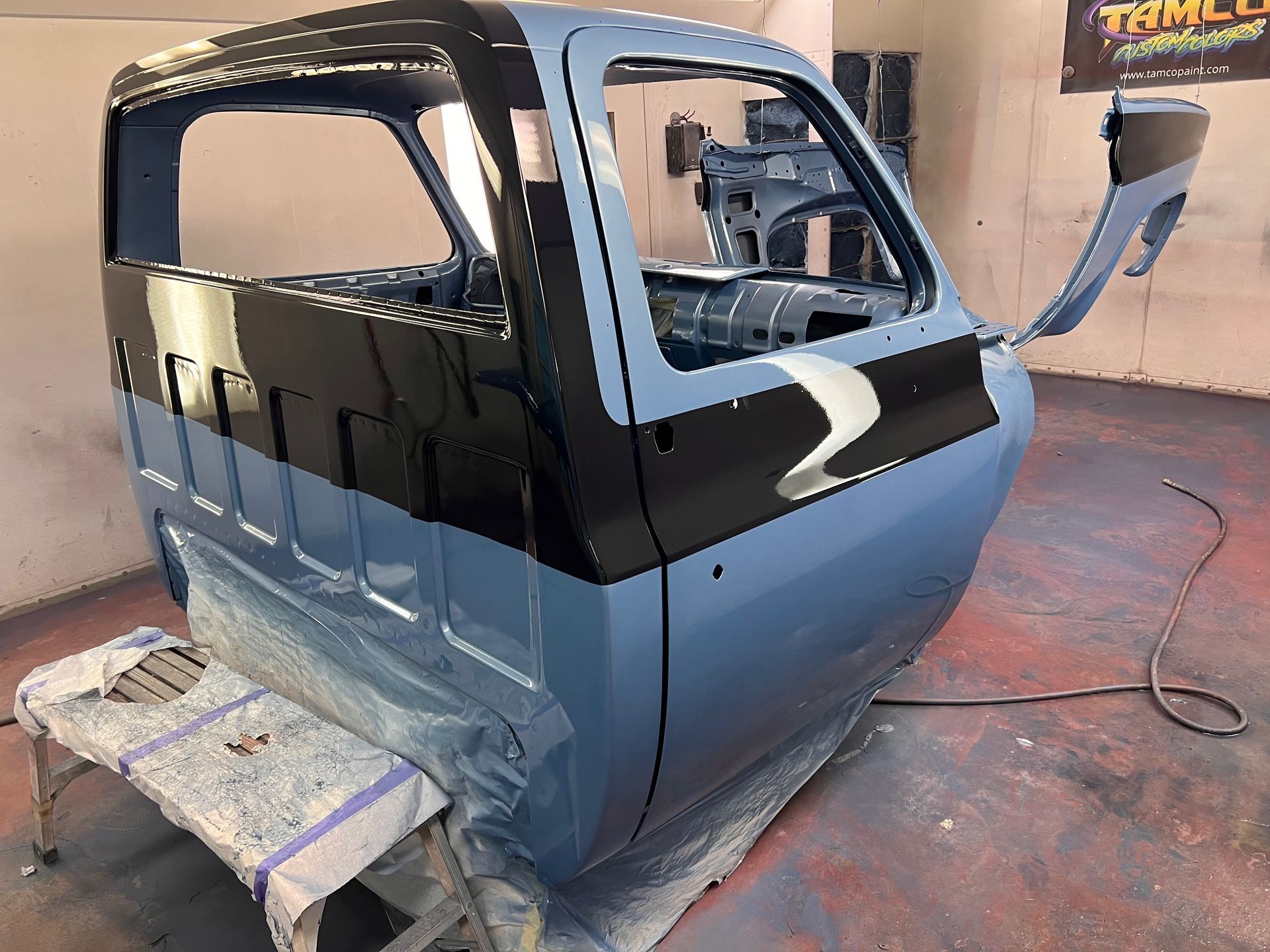 A blue truck is being painted in a garage.