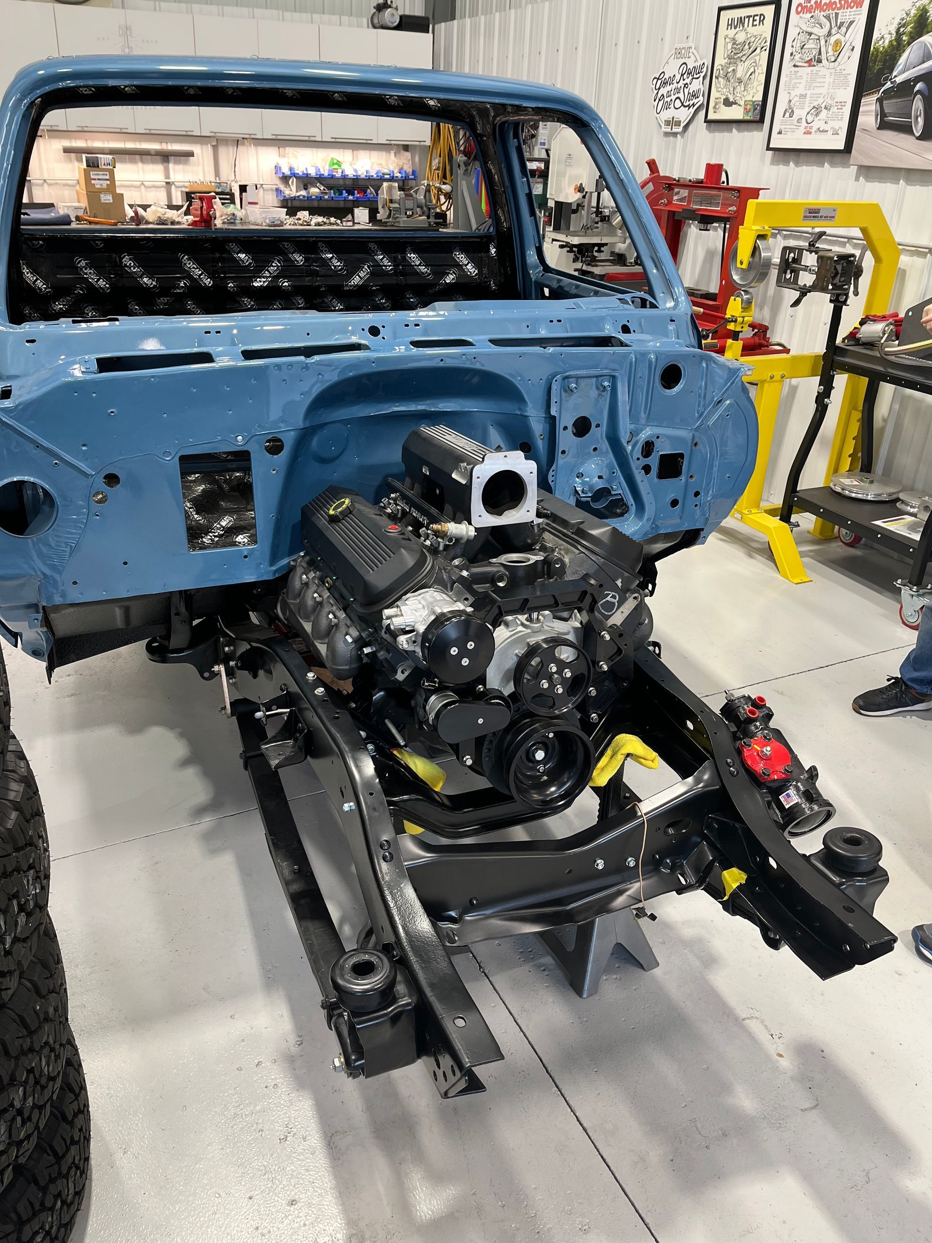 A blue truck with a black engine is being built in a garage.