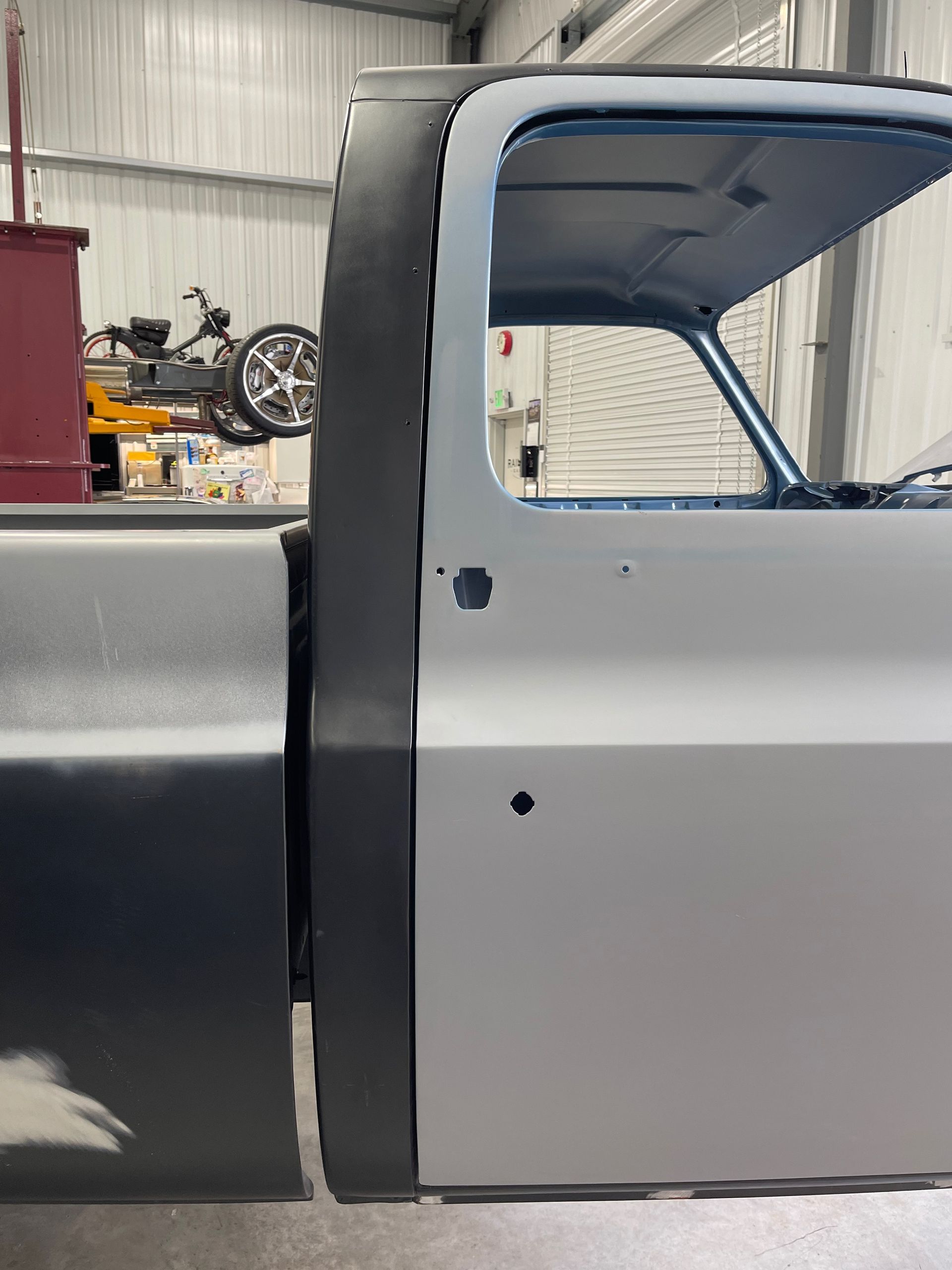 A truck is sitting in a garage with a motorcycle parked behind it.