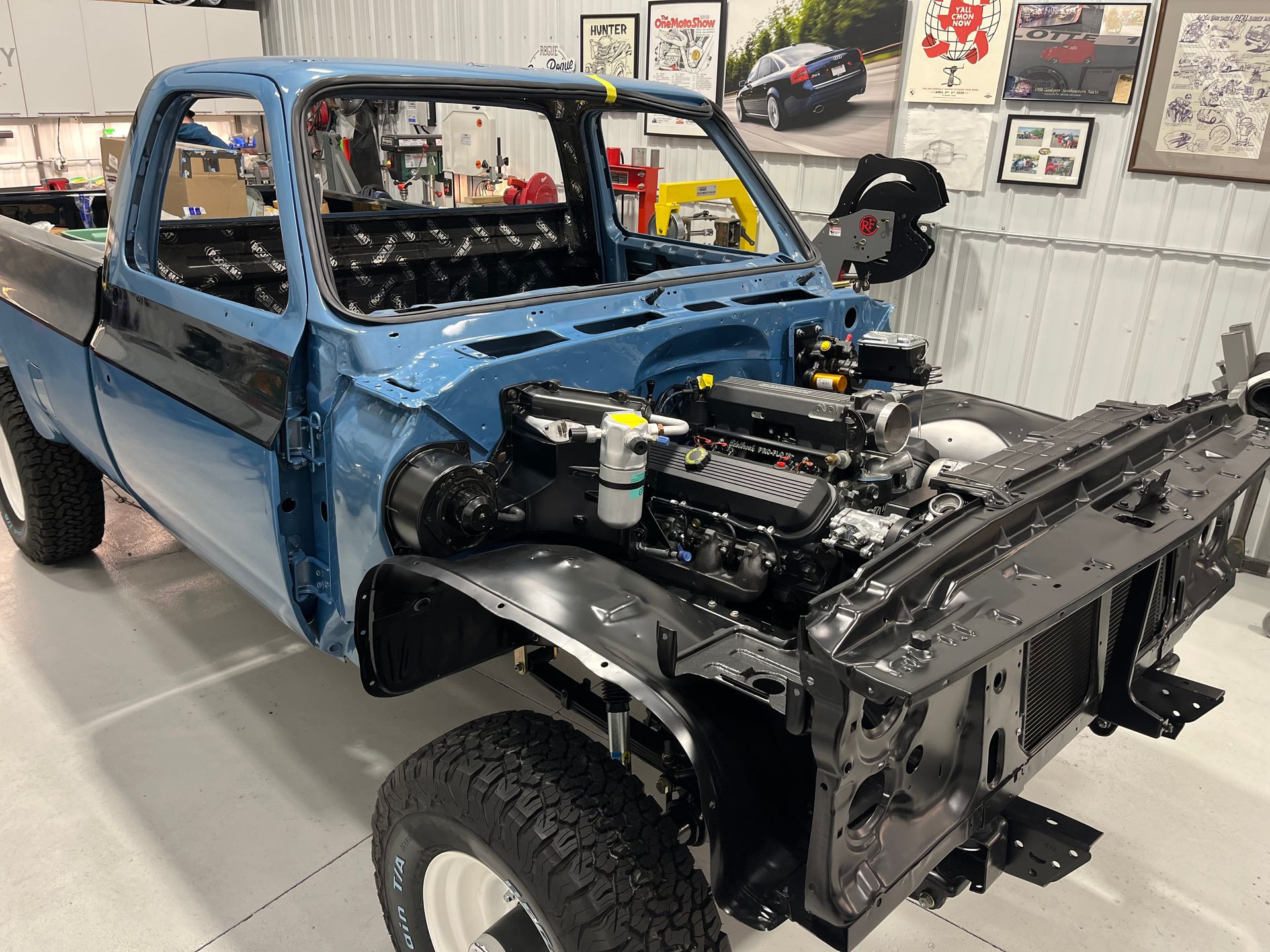 A blue truck is being built in a garage with the engine exposed.