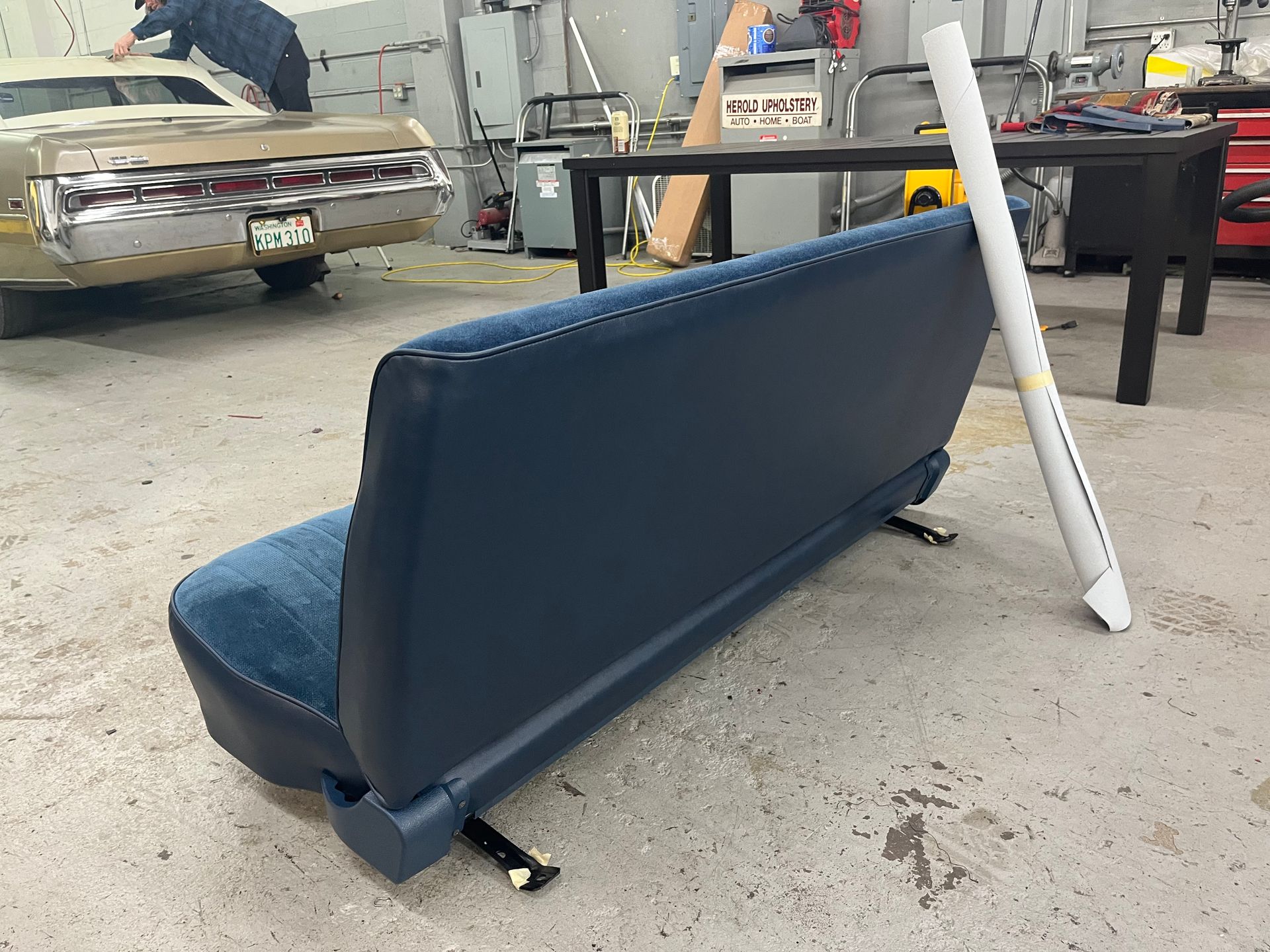 A blue couch in a garage with a car in the background