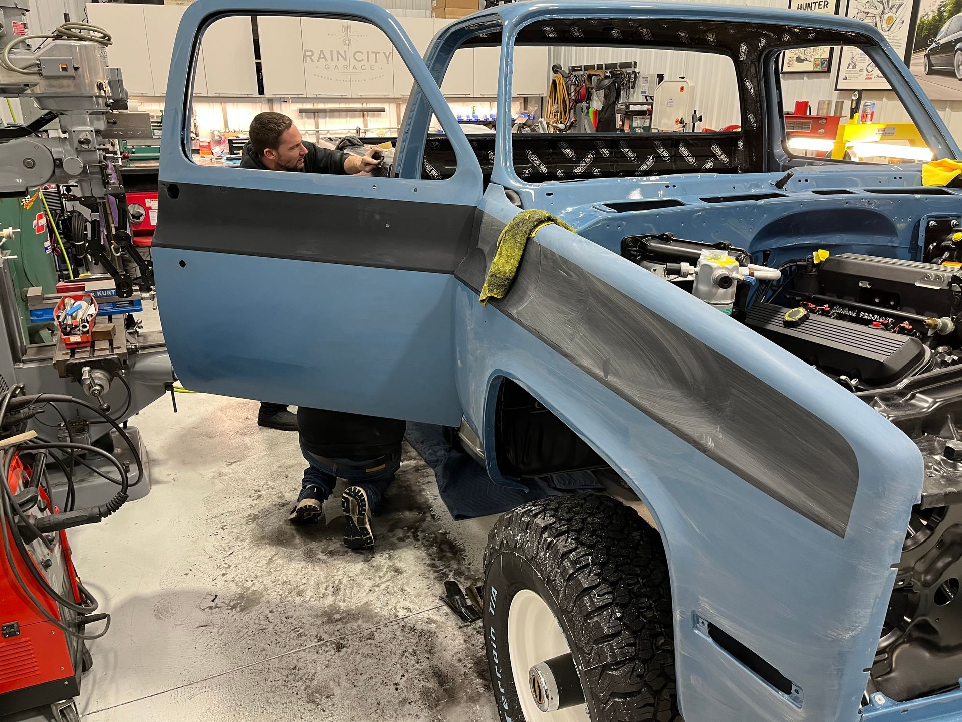 A man is working on a blue truck in a garage.