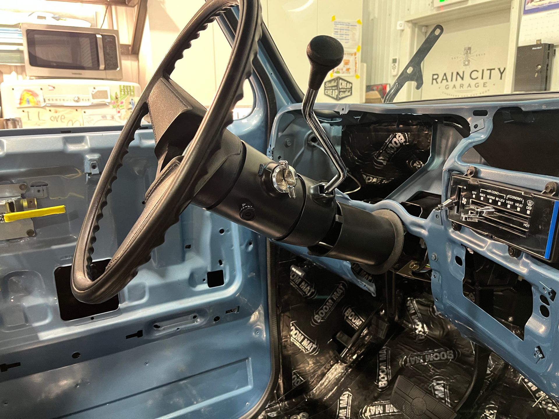 The inside of a blue truck with the door open and the steering wheel visible.