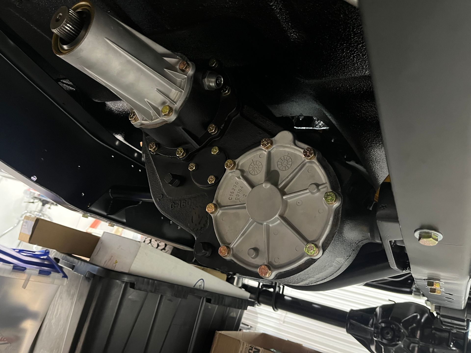 A close up of a gearbox under a car in a garage.