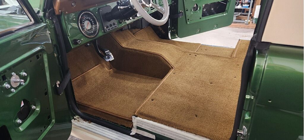 The interior of a green truck with a steering wheel and a carpeted floor.