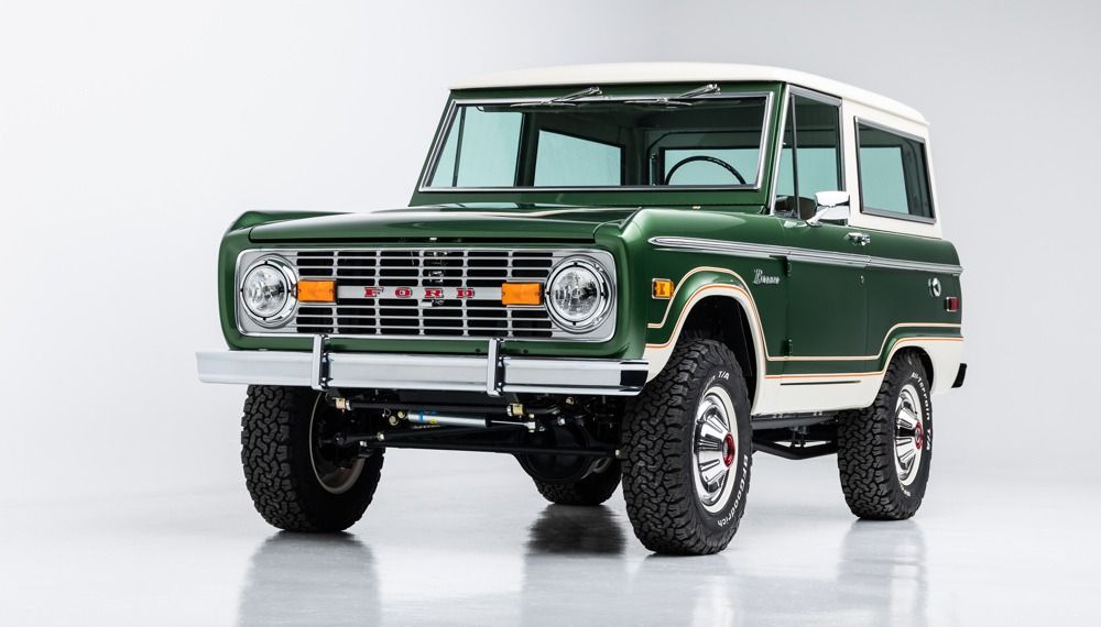 A green and white ford bronco is parked in front of a garage.