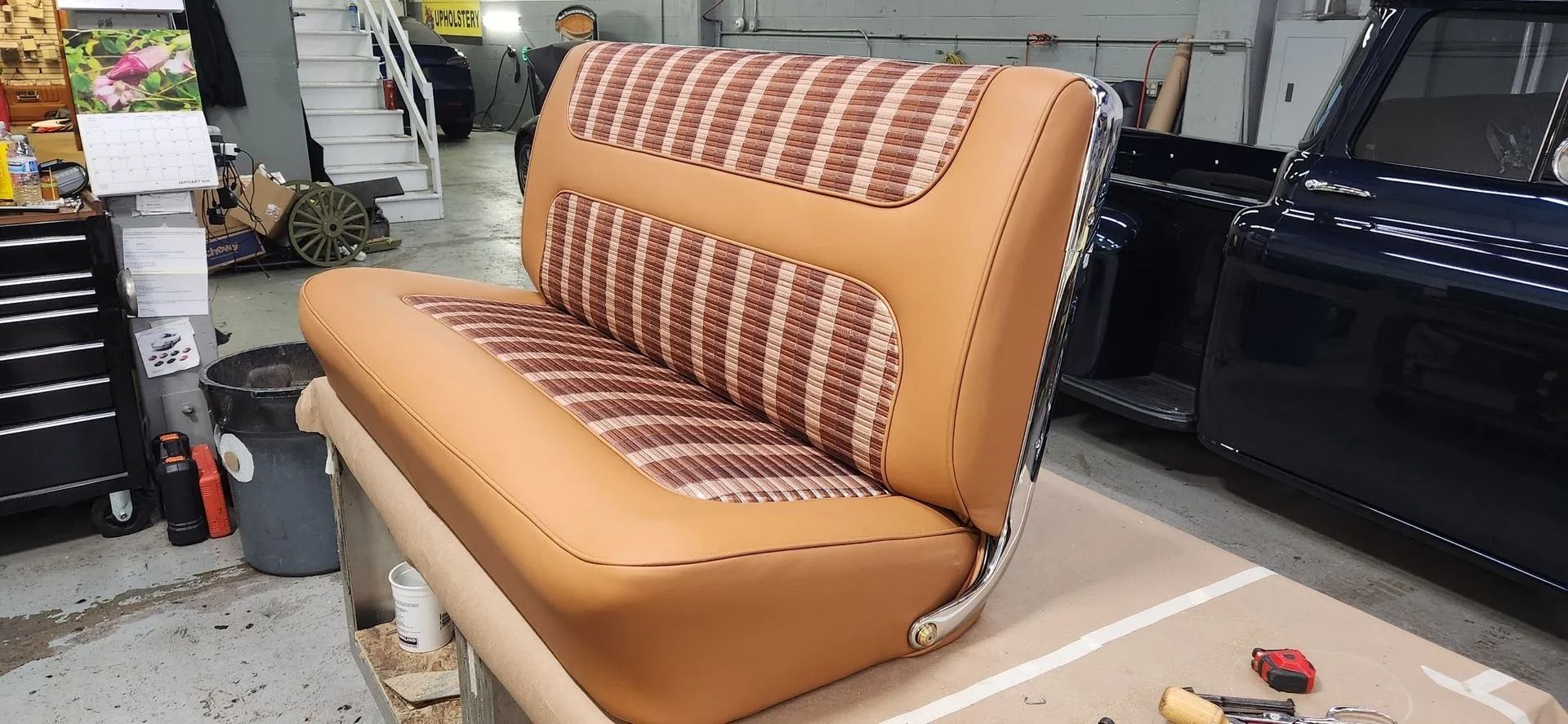 A brown couch is sitting on top of a table in a garage next to a car.