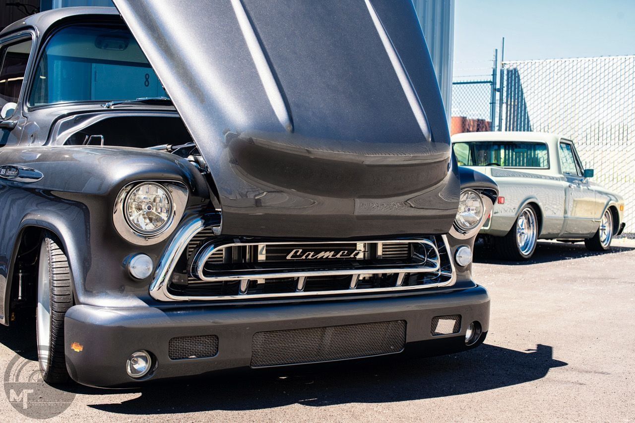 A truck with the hood up is parked next to another truck