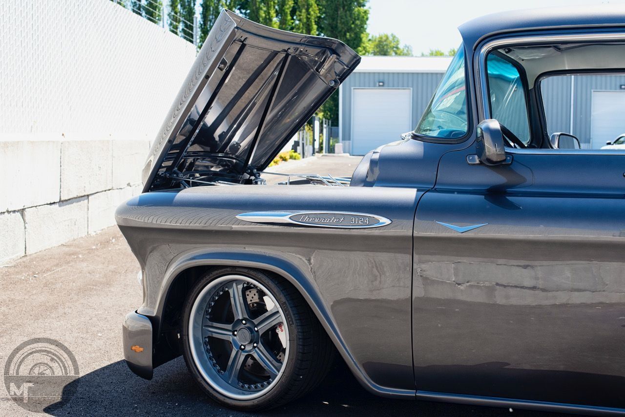 A black truck with the hood up is parked in a parking lot.