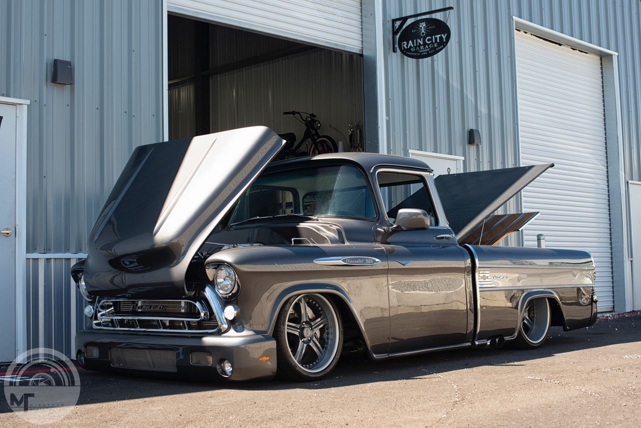 A truck with its hood up is parked in front of a building.