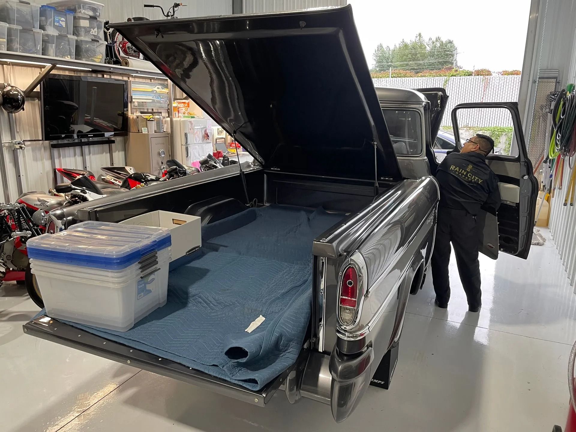 A man is standing next to a truck with the bed open in a garage.