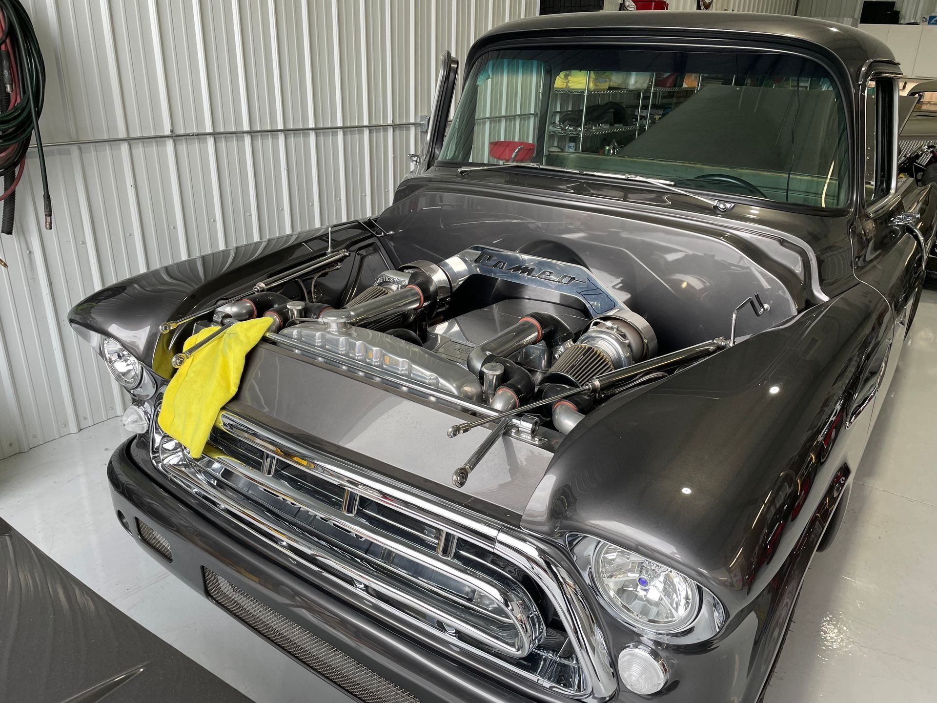 A gray truck with the hood open is sitting in a garage.