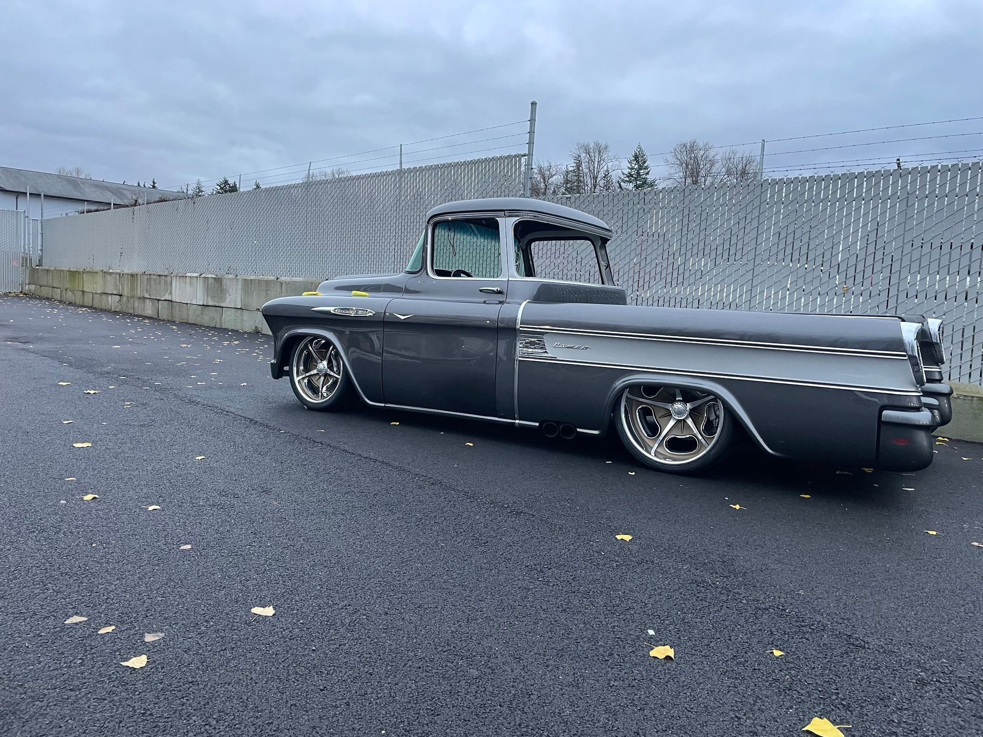A black truck is parked on the side of the road next to a fence.