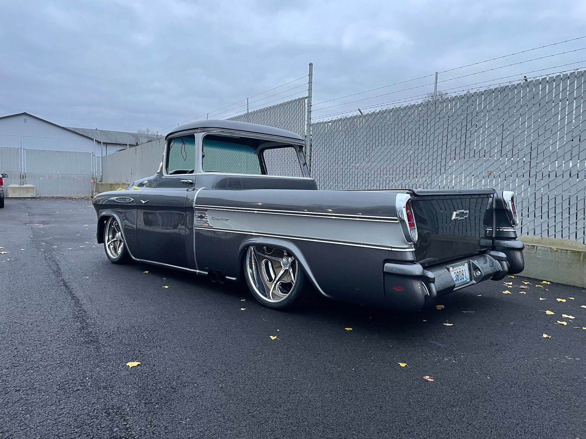 A black truck is parked in a parking lot next to a fence.