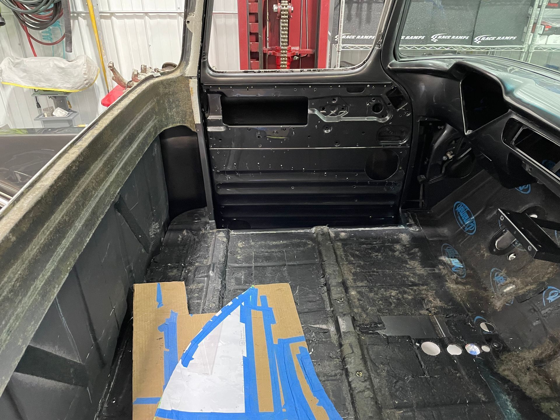 The back of a car is being painted and there is a piece of blue tape on the floor.