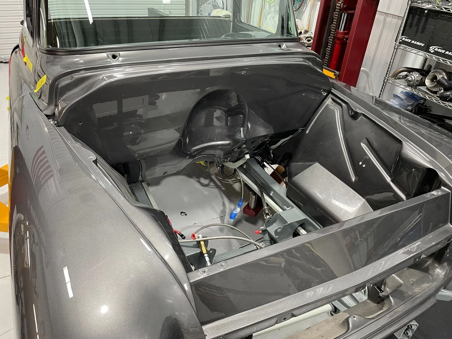 A gray car is being built in a garage with the hood open.
