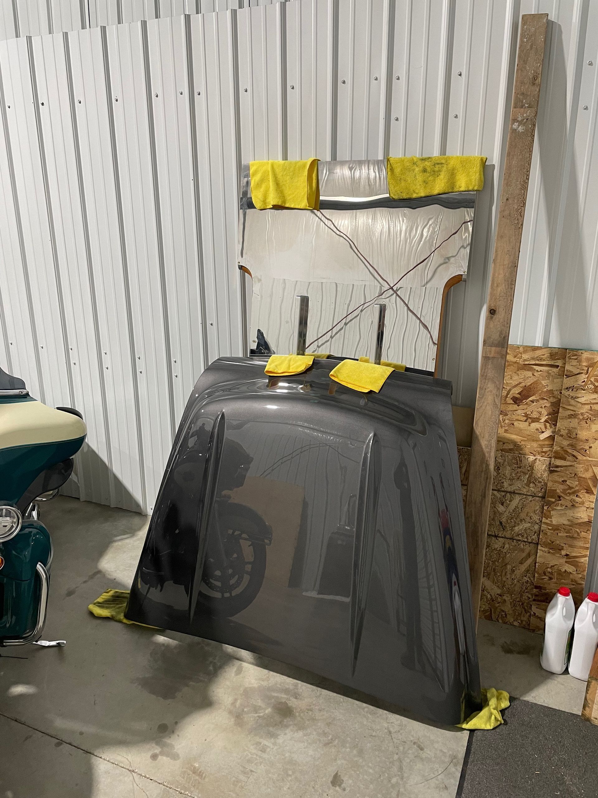 A hood is sitting on the ground in a garage next to a motorcycle.