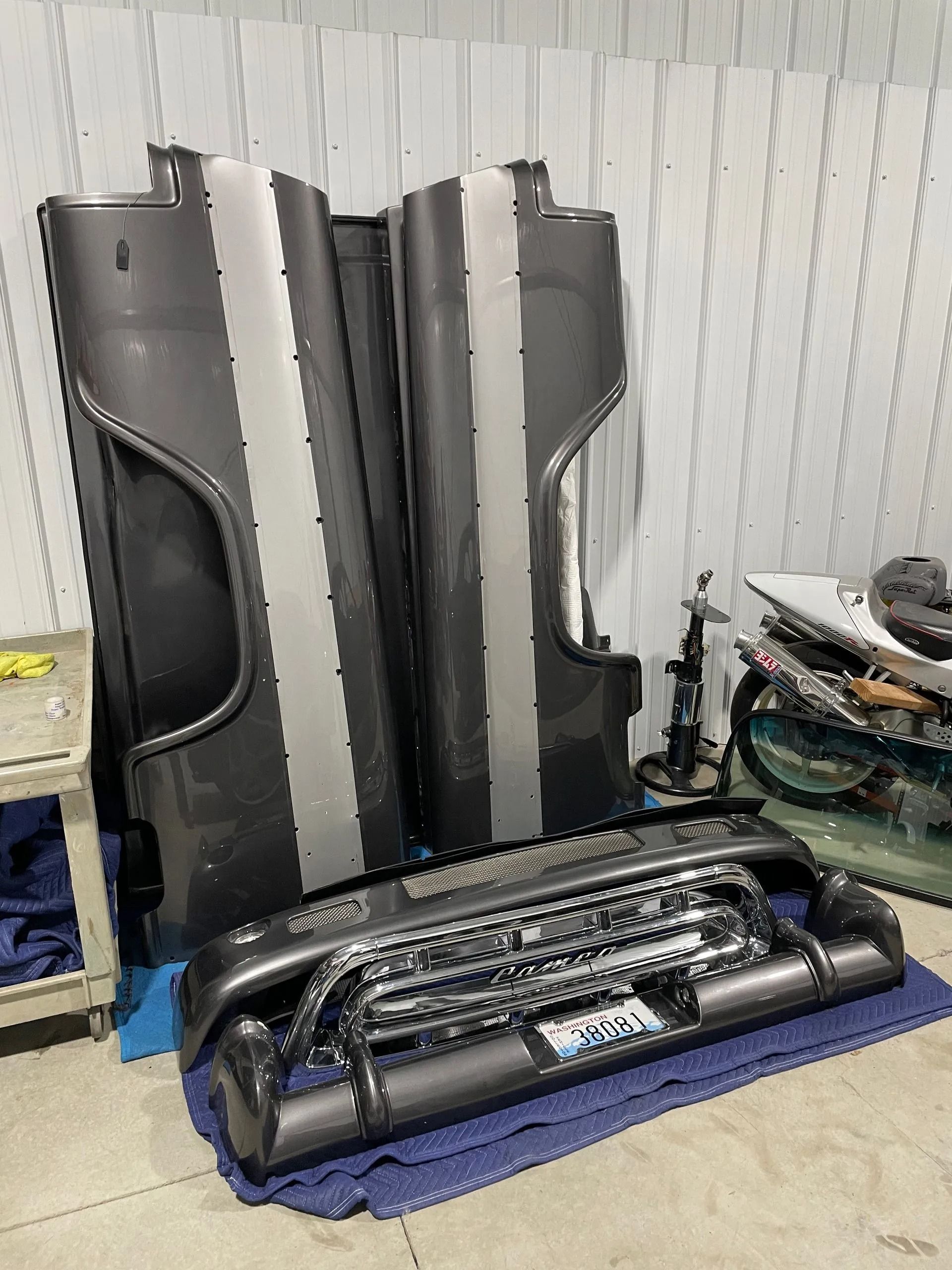 A bunch of car parts are sitting on the floor in a garage.