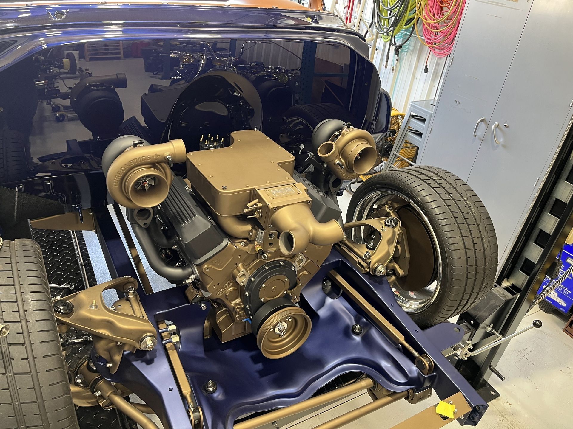 A blue car with a gold engine is sitting on a lift.