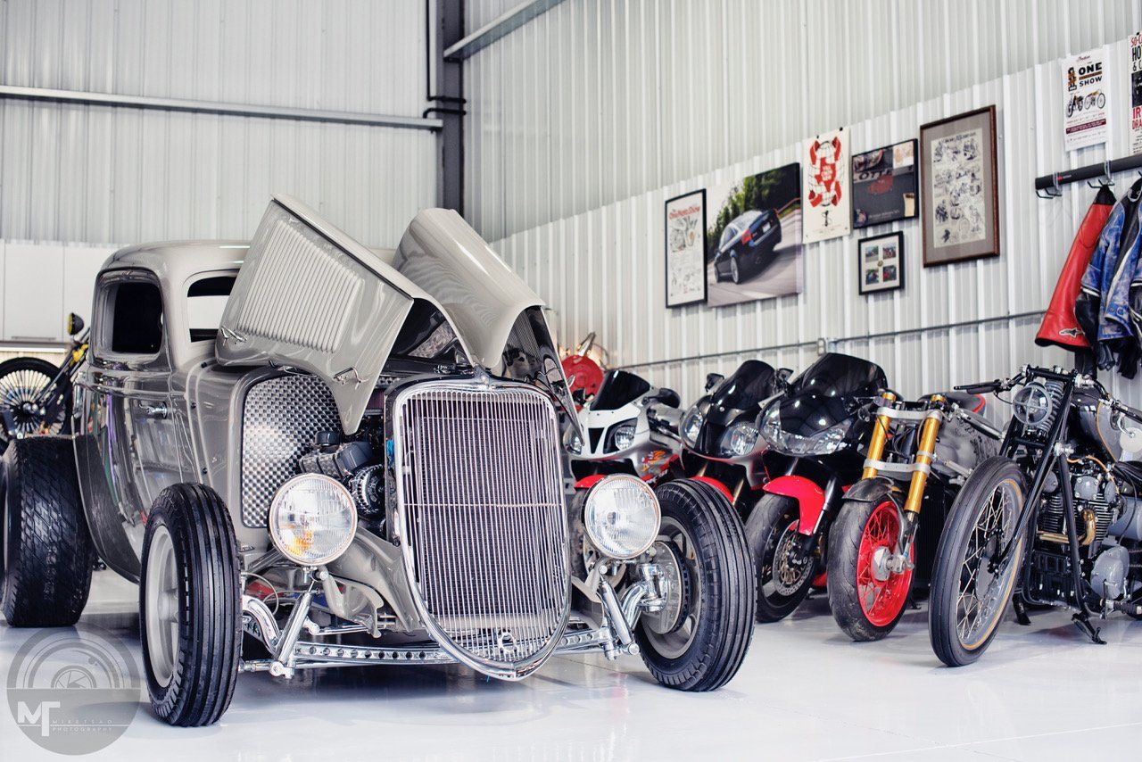 A hot rod is parked in a garage next to motorcycles.