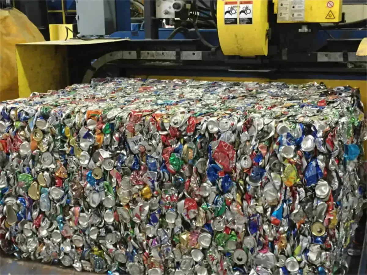 A large, dense, rectangular bale of crushed, colorful aluminum beverage cans sitting on industrial recycling machinery.