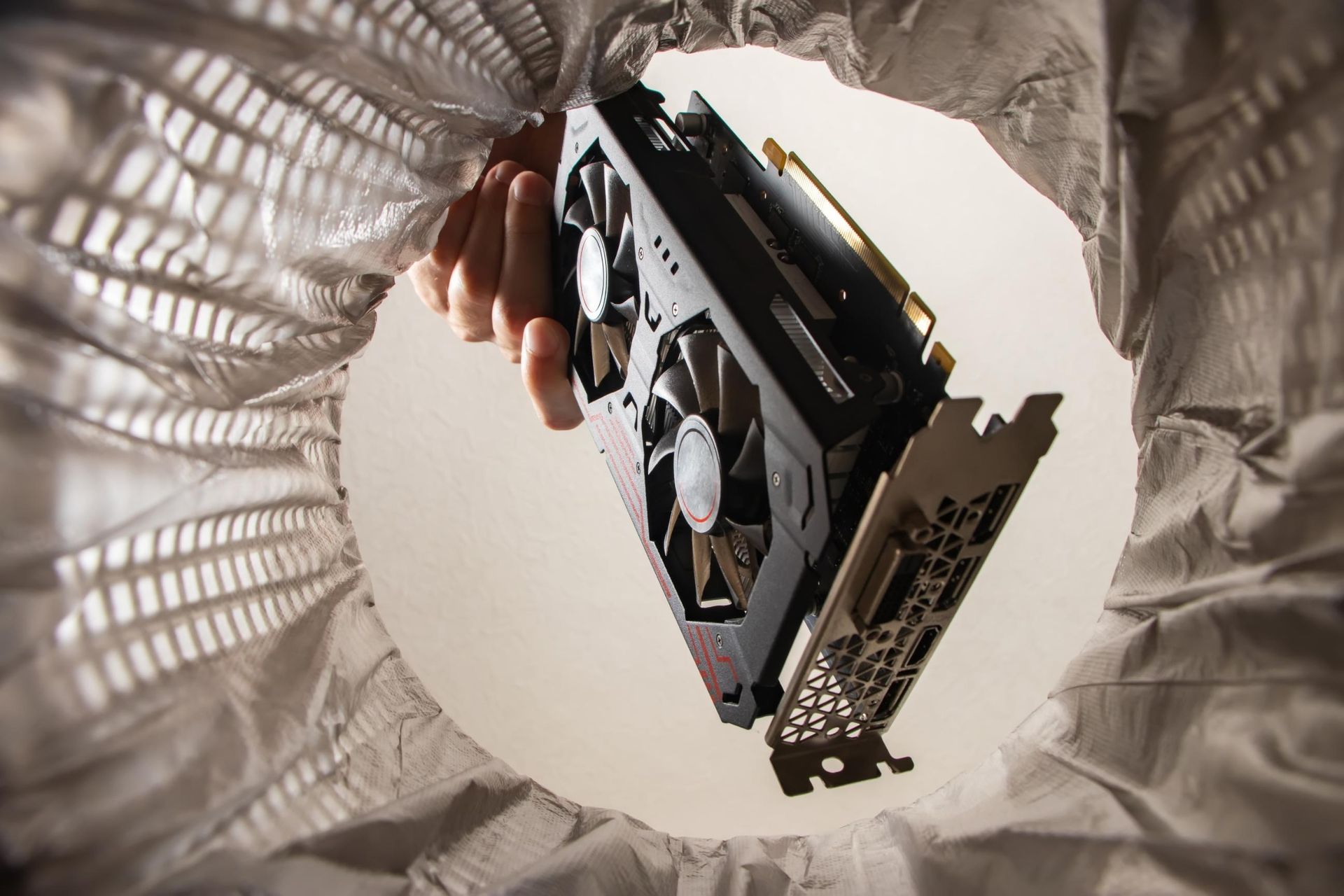 A hand dropping a computer graphics card into a wastebasket.
