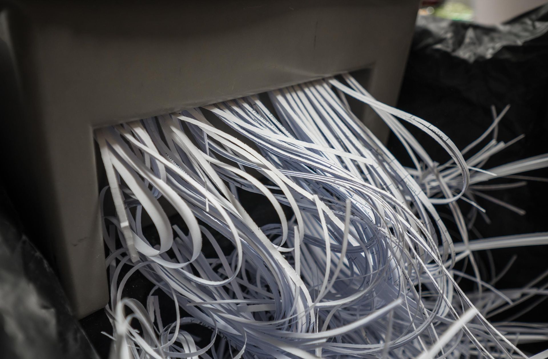 A paper shredder disposing of a thick stack of white cable ties into a black waste bin.