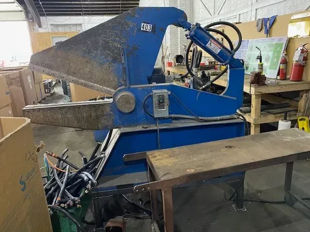 A blue metal cutting shear sits in an industrial workshop next to a workbench.