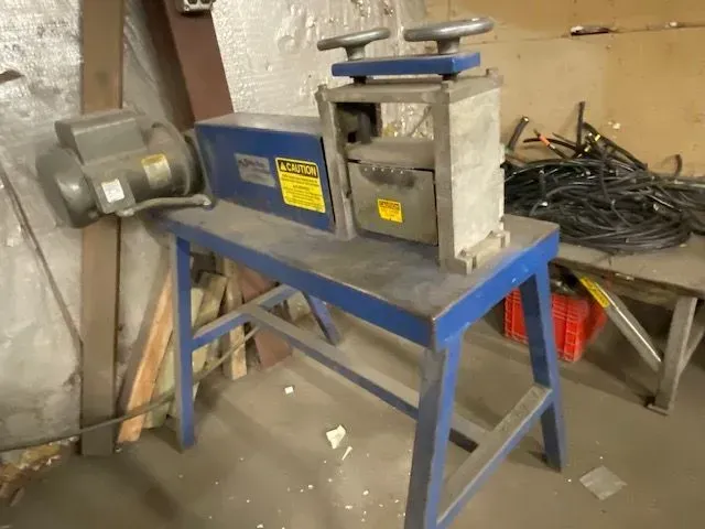 A blue, motorized wire stripping machine sits on a metal workbench in a cluttered workshop.