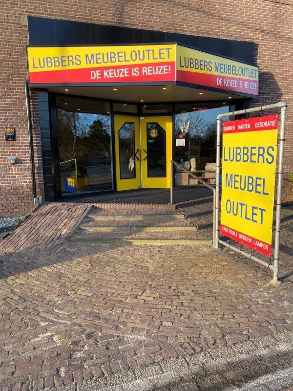Een bakstenen gebouw met een gele deur en een bord waarop staat lubbers meubel outlet