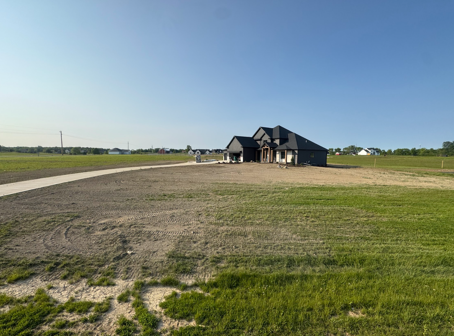 A new house under construction on a grassy lot with a walkway, under a clear blue sky.
